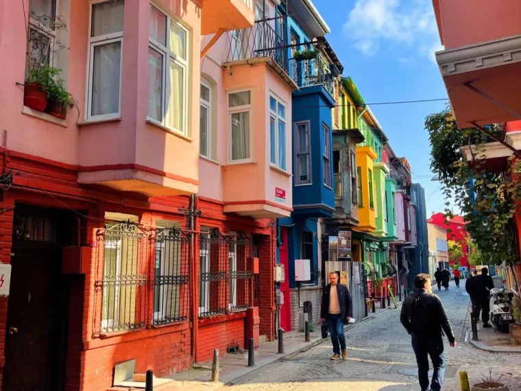 A narrow Balat street lined with pink, orange, yellow and blue houses under a bright sky