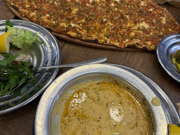 Lahmacun on a wooden board beside a bowl of mercimek soup and a green salad at the lunch stop
