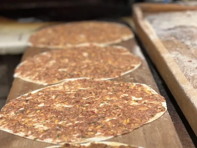 Rounds of raw lahmacun lined up on a board, waiting for the oven