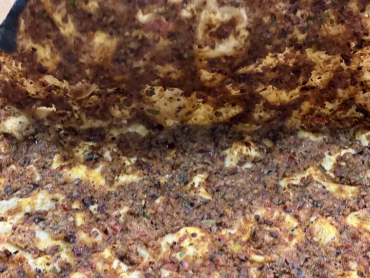 A lahmacun lifted straight from the oven, minced meat and herbs across the thin dough