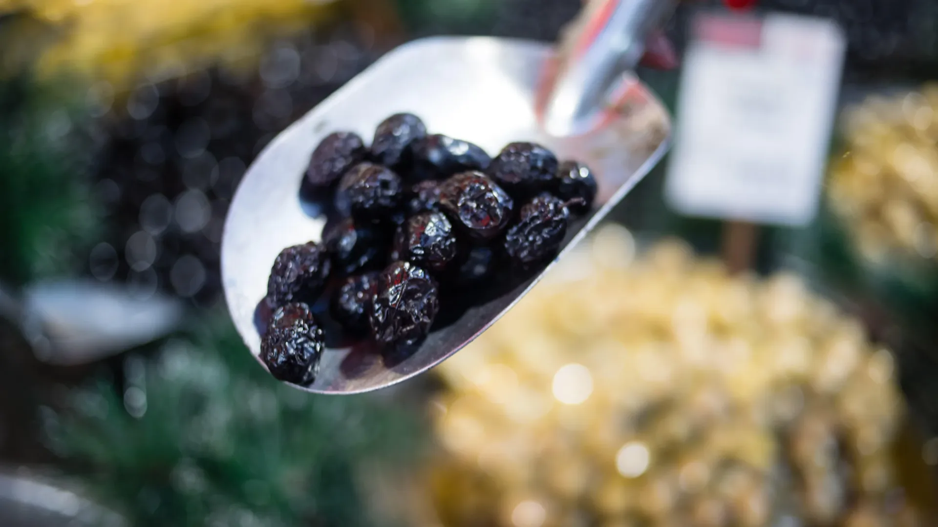 A scoop lifting black olives from the barrel at an Istanbul market stall