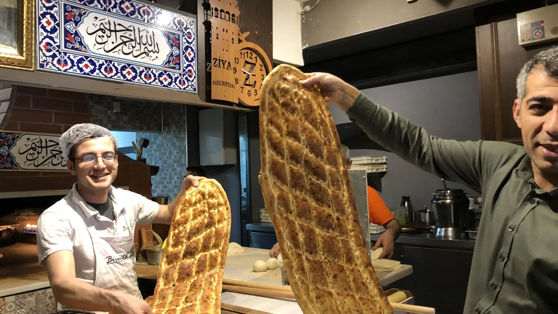Two bakers holding up long trays of freshly baked pide in an Istanbul bakery