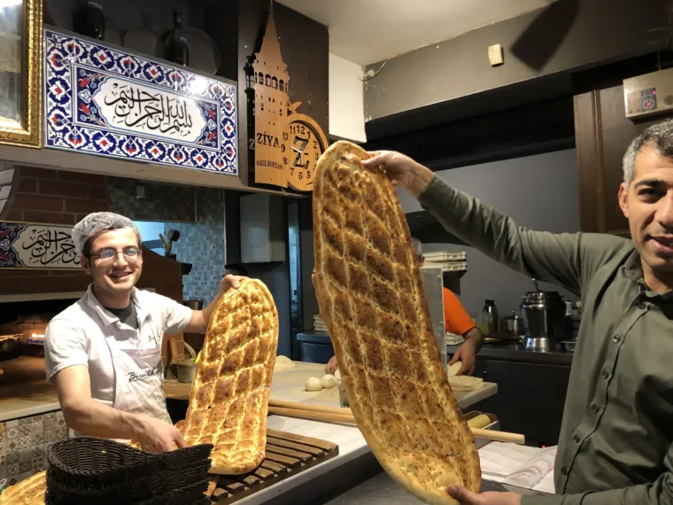 Two bakers holding up long trays of freshly baked pide in an Istanbul bakery