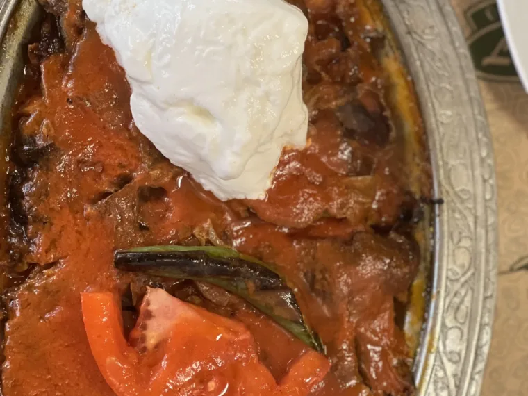 A copper tray of stew topped with yoghurt and a roasted pepper