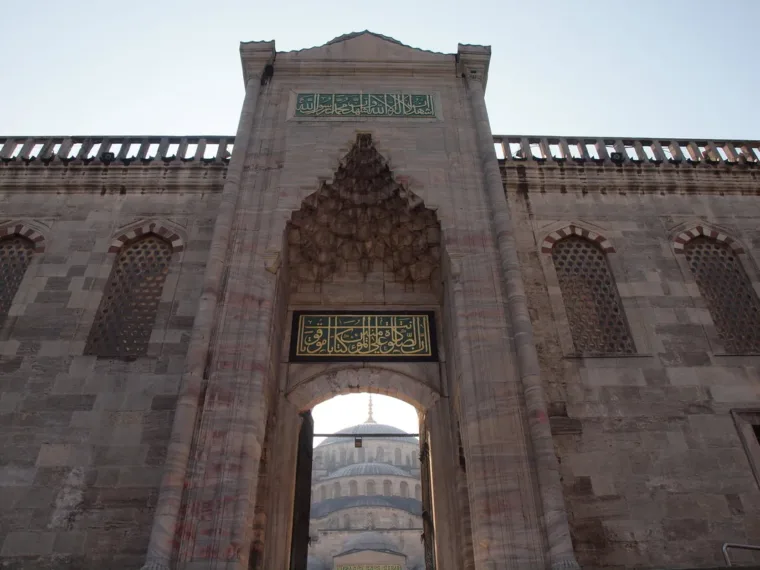 A monumental stone gateway with a tiled inscription panel, looking through to a domed courtyard