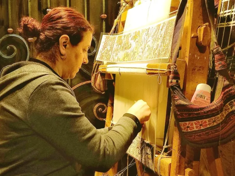 A weaver knotting a silk carpet at the loom, working from the pattern beside her