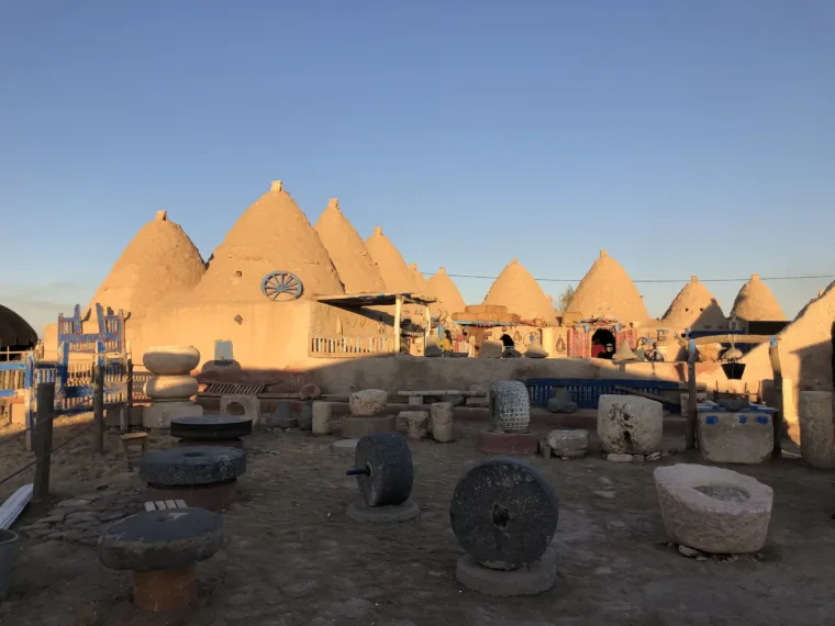 Old millstones and grinding wheels laid out in front of the Harran beehive houses