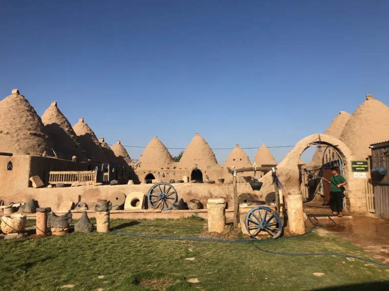 Carts and millstones on the grass in front of the Harran beehive houses