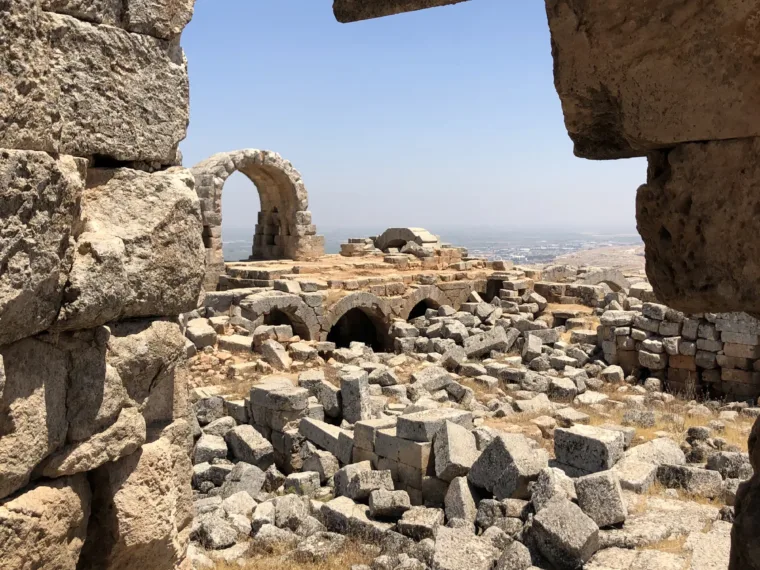 Fallen stone blocks and an arch on the hilltop ruins above the plain